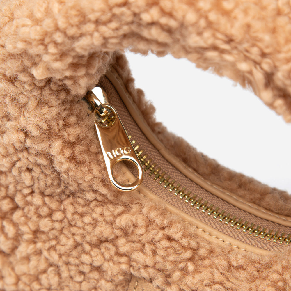 Close-up of a beige shearling bag with a gold zipper and 'UGG' logo.