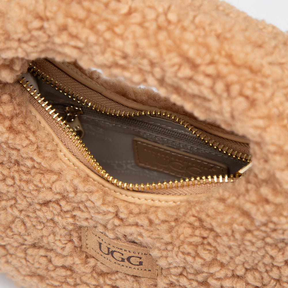 Close-up of a beige shearling bag with a zipper and UGG label.