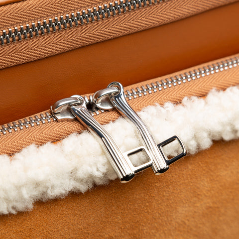 Close-up of a brown leather bag with a silver zipper and white fur lining.