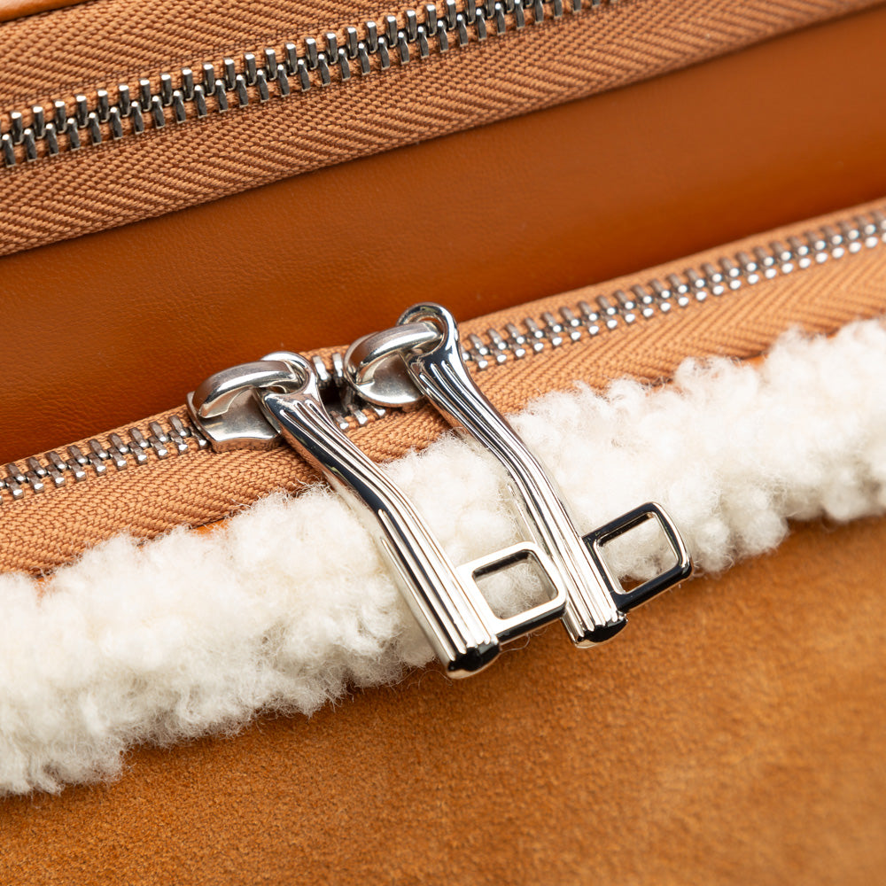 Close-up of a brown leather bag with a silver zipper and white fur lining.